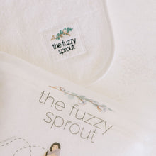 Load image into Gallery viewer, picture of the packaging of the fuzzy sprout&#39;s handsfree wearable baby towel and the logo on the towel
